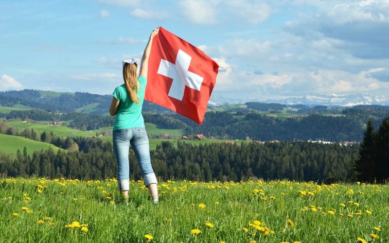 Femme agitant le drapeau suisse dans une campagne. 