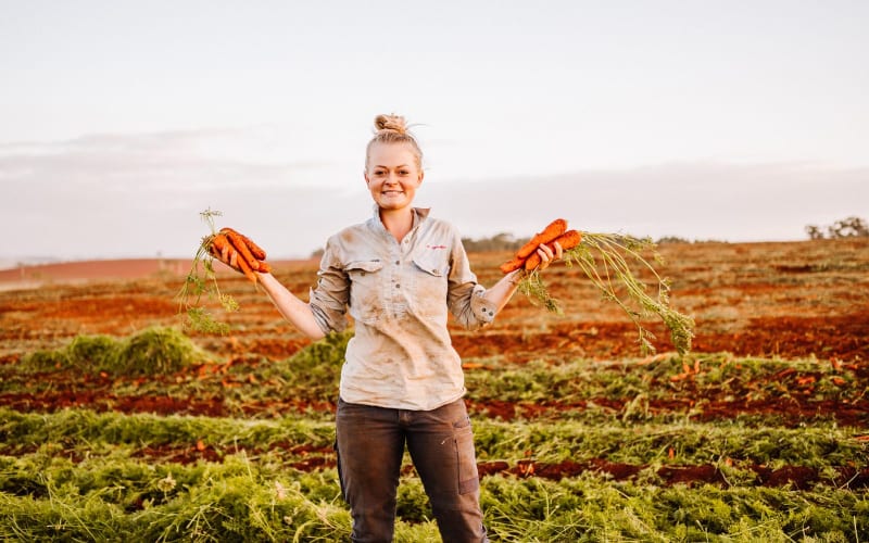Une femme heureuse en Australie en train de récolter des carottes. 