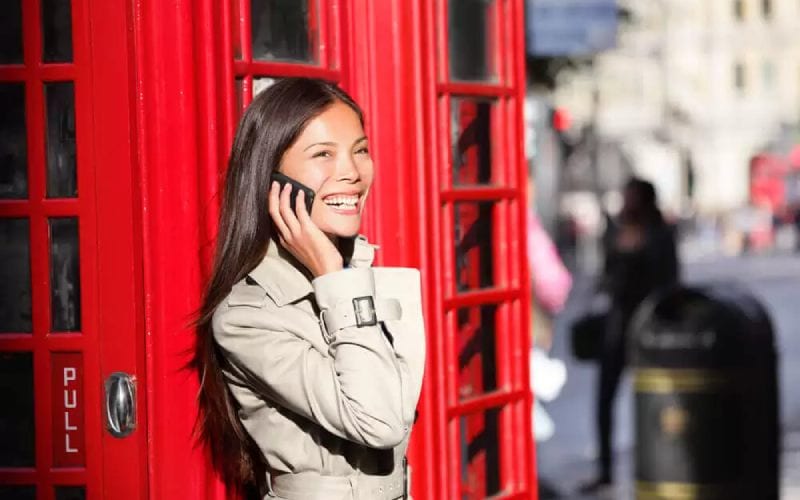 Une femme au téléphone en Angleterre près d'une cabinet téléphonique rouge. 