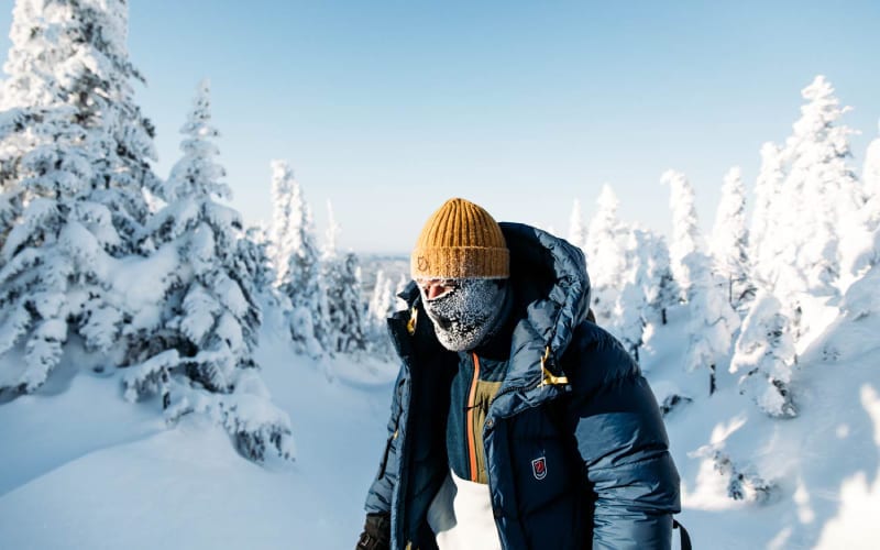 Un homme ayant froid et étant couvert dans une forêt enneigée. 